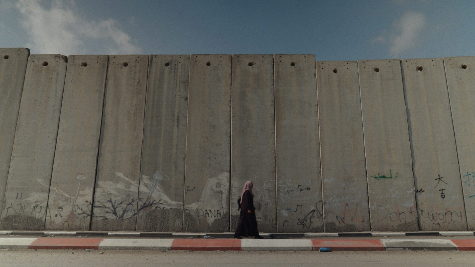 A woman walking by the wall — still from FOR LIFE